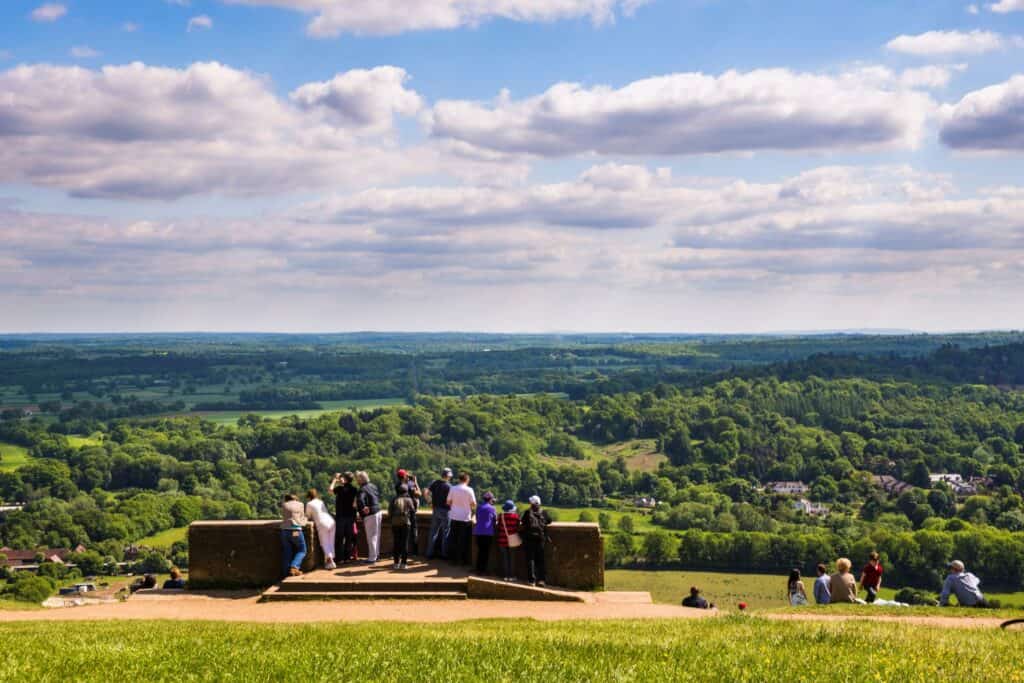 A group of people overlooking a scenic countryside from a lookout point on a bright, sunny day.
